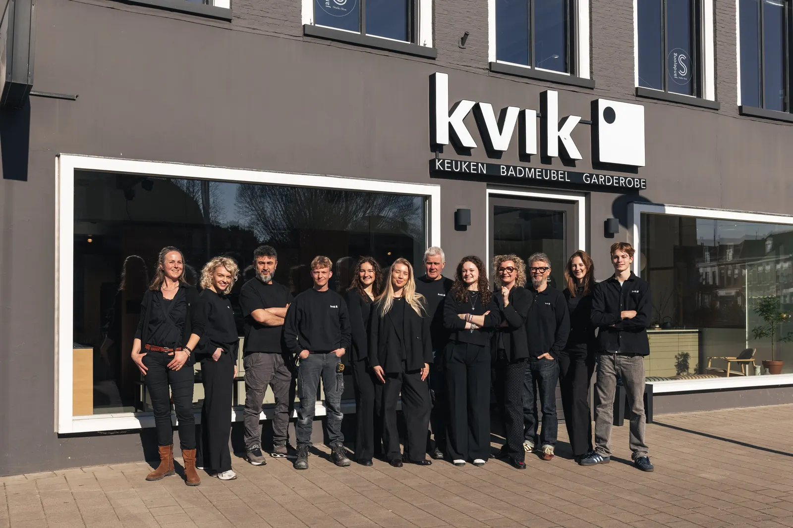 Het team van Kvik Leeuwarden, in het zwart gekleed, op een rij voor de winkel aan de Schrans